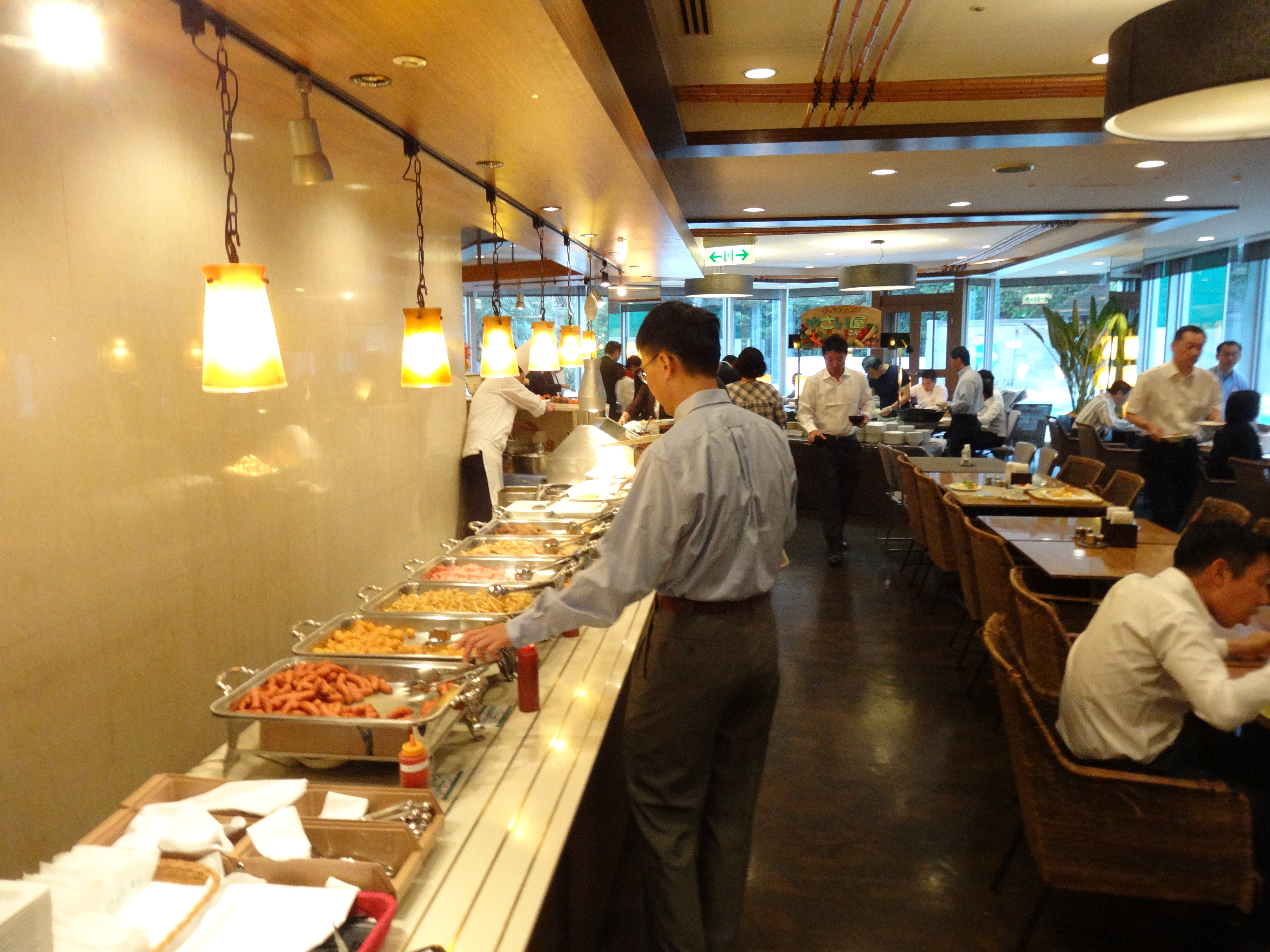 料理カウンターで食事を選ぶ人がいるビュッフェ会場の写真